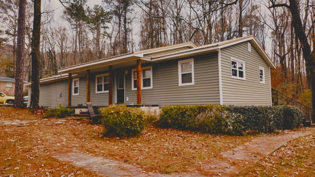 Charming gray house with porch, surrounded by trees and autumn leaves, inviting neighborhood setting.